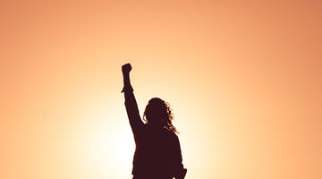 A woman holds up a fist in front of the sunset. 